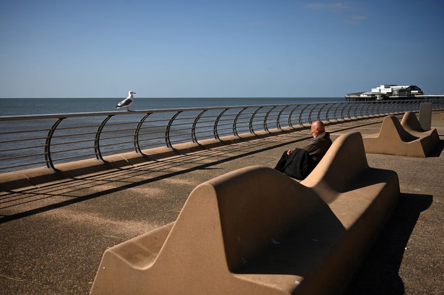  A seagull perches on a railing near a man sitting and looking at the sea, near the central pier in the spring sunshine on the coast in Blackpool, north-west England on April 13, 2020, during the nationwide lockdown to combat the novel coronavirus pandemic. - AFP