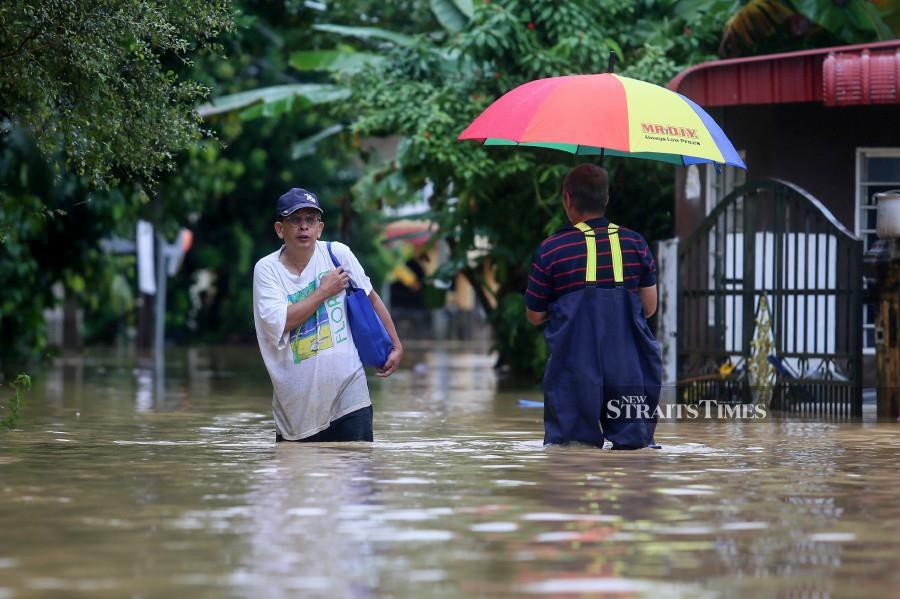 Locals wade through the floods waters in Kampung Pulau Rusa, Kuala Terengganu. - NSTP/GHAZALI KORI
