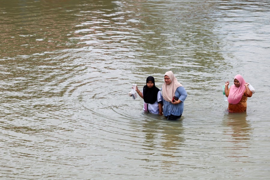 Flood victims wade through the floodwaters to reach the SK Kedai Tanjung relief centre in Pasir Mas. - BERNAMA PIC