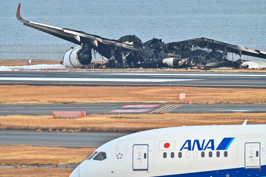 An All Nippon Airlines (ANA) plane taxis past the burnt wreckage of a Japan Airlines (JAL) passenger plane on the tarmac at Tokyo International Airport at Haneda in Tokyo. - AFP PIC
