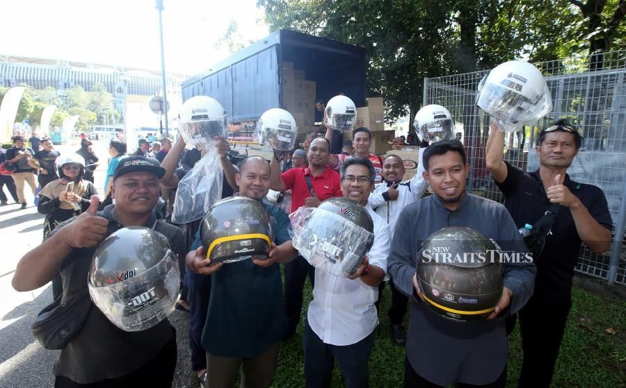 Delighted motorists showing their new motorcycle helmets during the Madani Government One Year Anniversary Programme in Bukit Jalil. -NSTP/HAIRUL ANUAR RAHIM