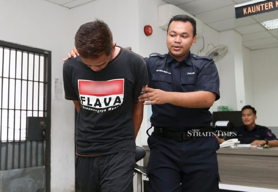 Mohd Fauzan Mat Ali is escorted by a policeman ahead of the trial at the Kota Baru Session’s Court. -NSTP/NIK ABDULLAH NIK OMAR