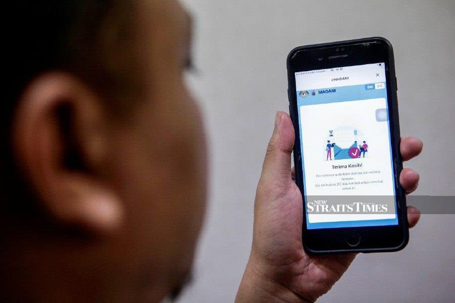 A man uses his smartphone to redeem eMadani credit in Putrajaya this morning. -NSTP/AIZUDDIN SAAD