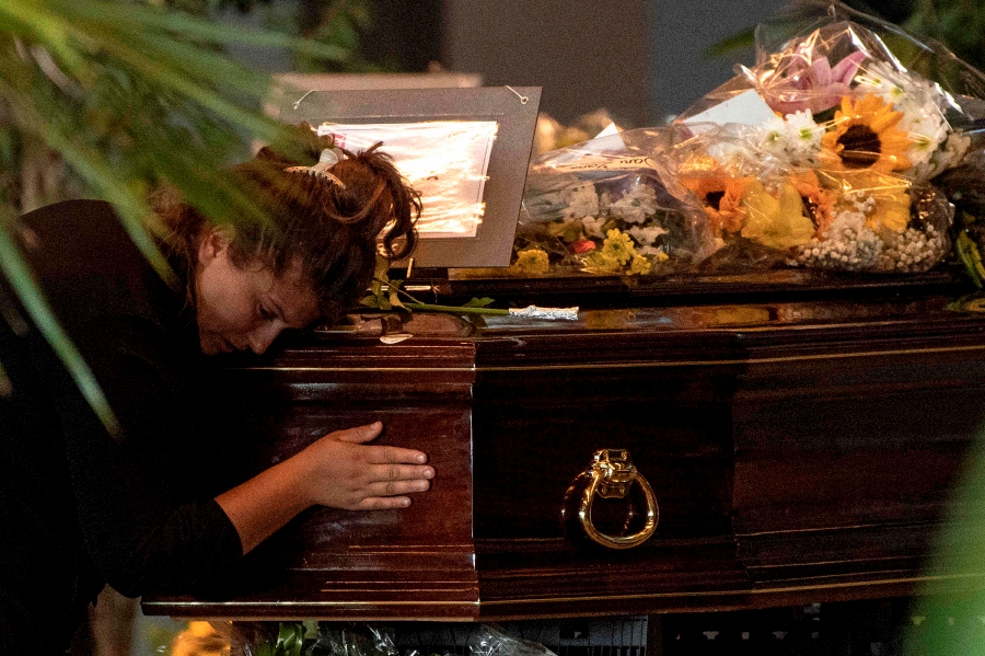 TOPSHOT - A mourner prays at the coffin of a victim of the Morandi bridge collapse in Genoa, on August 17, 2018. - Grieving relatives wept over coffins of dozens of victims of Genoa's bridge collapse on August 17, 2018, as controversy clouded a planned state funeral, while rescuers pressed on with their formidable search for those missing in the rubble. Fury is growing over the shock collapse of the Morandi bridge, a decades-old viaduct that crumbled in a storm on August 14 killing at least 38 people, with Italian media reporting that some outraged families would shun August 19's official commemorations. — AFP pic 