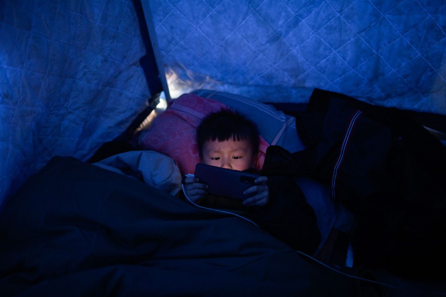 An earthquake survivor holds a mobile phone at a makeshift shelter made of tarpaulin in Jishishan County in northwest China's Gansu province. - AFP PIC
