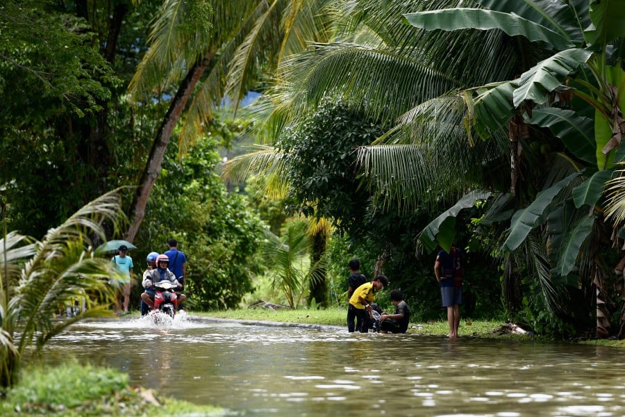 Residents of Taman Malihah wade through the floodwaters following heavy rain in Kuching. - BERNAMA PIC