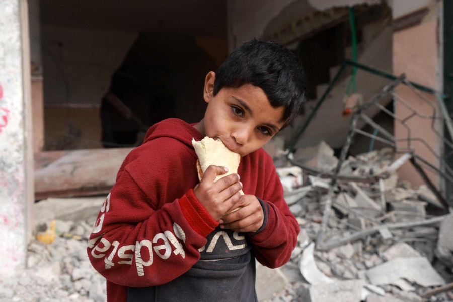 A child eats a sandwich as he stands in front of a building damaged by Israeli bombardment in Rafah in the southern Gaza Strip. - AFP PIC