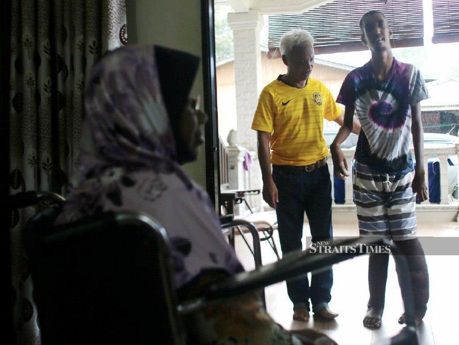 Ramli Mamat (in yellow) with his son Mohammad Arif Hakimi while his wife, Murni Md Daud, looks on at their house in Kampung Bukit Palas near Cherating here. - NSTP/FARIZUL HAFIZ AWANG 
