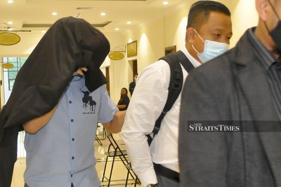 Mohd Hizan Laliman covers his face as he led out of the Special Corruption Court in Kota Kinabalu. - NSTP/MOHD ADAM ARININ