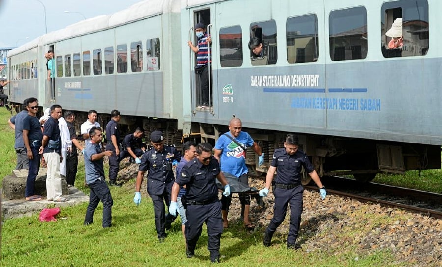   Police personnel carry Lena Gabin’s remains after she was hit by a train from Putatan heading to Kota Kinabalu. — NSTP/JUWAN RIDUAN