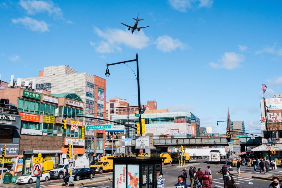 An airplane flies over stores on Main Street in the Flushing neighborhood in the Queens borough of New York, U.S., on Monday, March 29, 2021. The U.S. economy is on a multi-speed track as minorities in some cities find themselves left behind by the overall boom in hiring, according to a Bloomberg analysis of about a dozen metro areas.