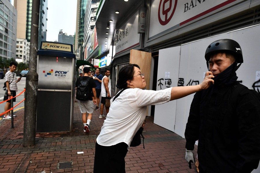 A woman tries to remove a facemask worn by a protesters after an anti-emergency law march from the Tsim Sha Tsui to Sham Shui Po areas of Hong Kong. - AFP