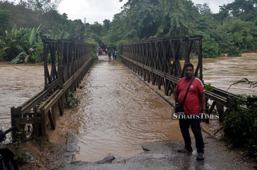 An Orang Asli showing the Sungai Betis bridge inundated with floodwaters in Gua Musang. - BERNAMA PIC