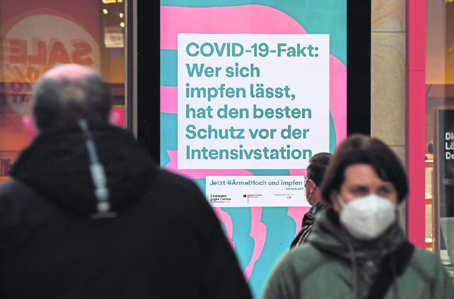 People walking past a sign that reads “Covid-19-fact: those who get vaccinated have the best protection against the Intensive Care Unit” in Dortmund, Germany, on Jan 13. -AFP PIC