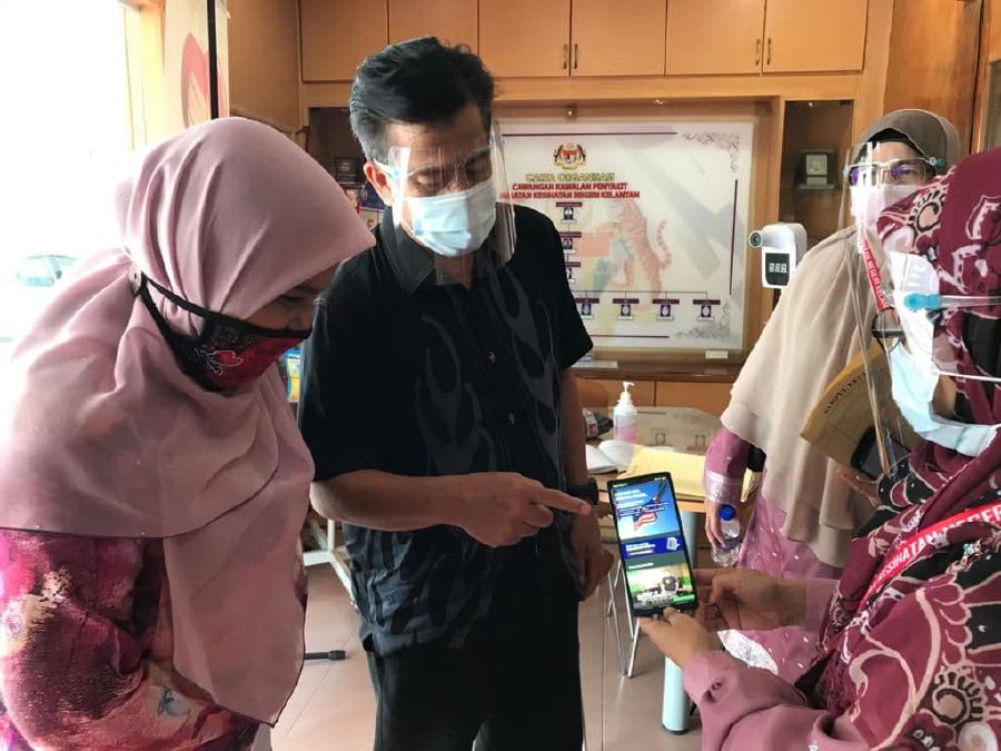 Kelantan health director Datuk Dr Zaini Hussin (centre) looking at the Mysejahtera application used to register for the Covid-19 vaccination. - Pic by Sharifah Mahsinah Abdullah