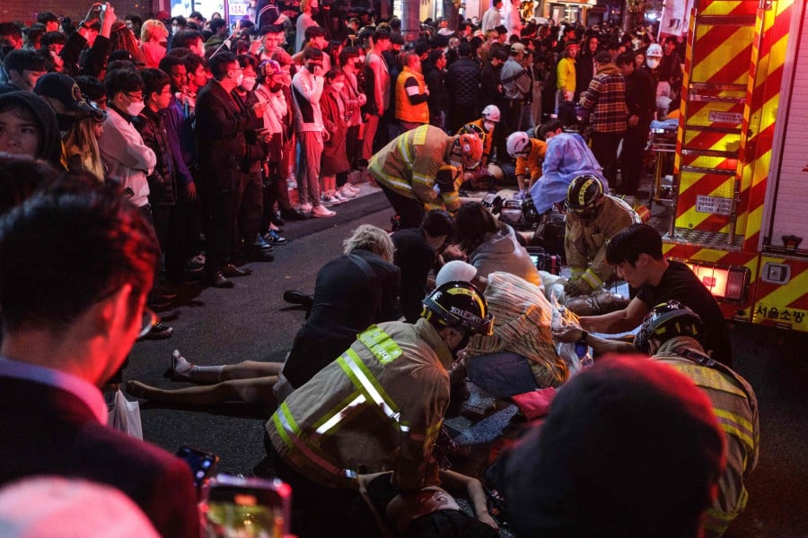 This picture taken on October 29, 2022 shows onlookers watching as emergency workers tend to people who were in a Halloween stampede in the district of Itaewon in Seoul. -AFP PIC