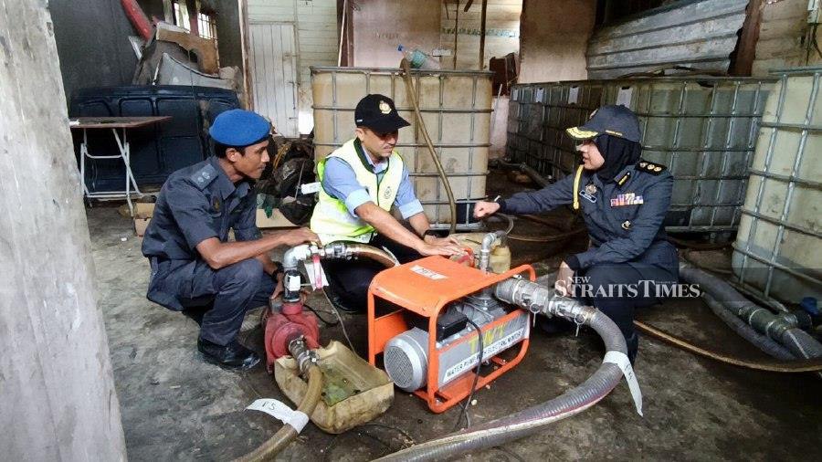 Kedah Domestic Trade and Cost of Living Ministry director Muhammad Nizam Jamaludin (centre), examines a modified pump used to easily siphon diesel fuel from the storage tank into trucks. - NSTP pic