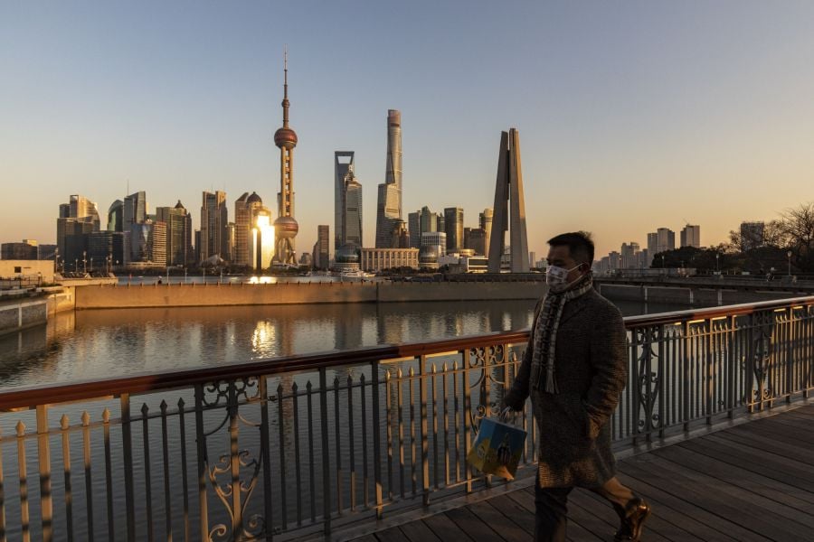 A pedestrian walks on a bridge past buildings in the Lujiazui Financial District across the Huangpu River in Shanghai, China, on Tuesday, Dec. 28, 2021. China’s economy expanded at a moderate pace in the final month of the year, supported by better business sentiment, easing factory inflation pressures and faster car sales. However the slumping property sector and slowing external demand are clouding the outlook for the world’s second-largest economy. Photographer: Qilai Shen/Bloomberg