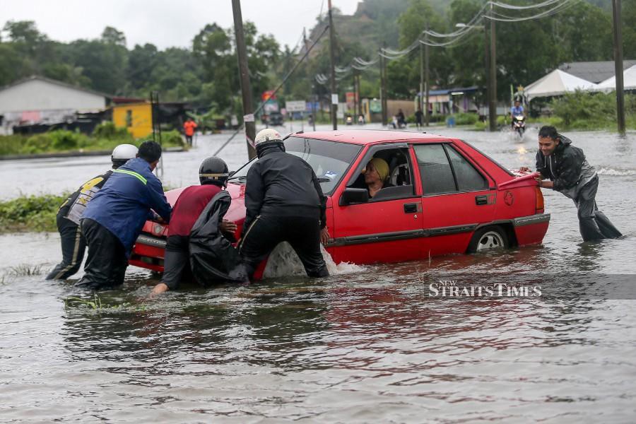Residents from Kampung Alor, Surau Panjang, help a motorist move his car which was stranded in the flood waters. - NSTP/GHAZALI KORI