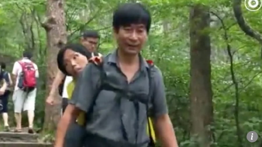 A husband has been filmed carrying his wife, who suffers from motor neurone disease, on his back up one of China’s most famous mountains. (pic from SCMP)