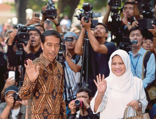 Indonesian presidential candidate Joko Widodo (L) and his wife Iriana Widodo (R) wave before voting at polling centre in Jakarta on July 9, 2014. Widodo declared victory on July 9 in Indonesia's tightest and most divisive presidential race since the downfall of dictator Suharto, which has pitted him against ex-general Prabowo Subianto.AFP