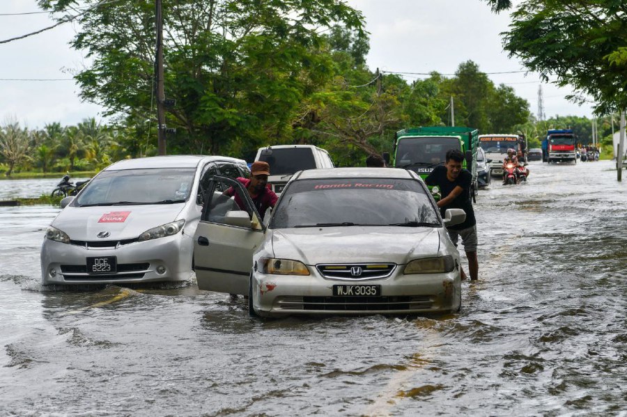 BACHOK: A driver and his passenger push their car through flood waters near Kampung Sri Sentosa following heavy rainfall since Wednesday (November 29). -BERNAMA PIC