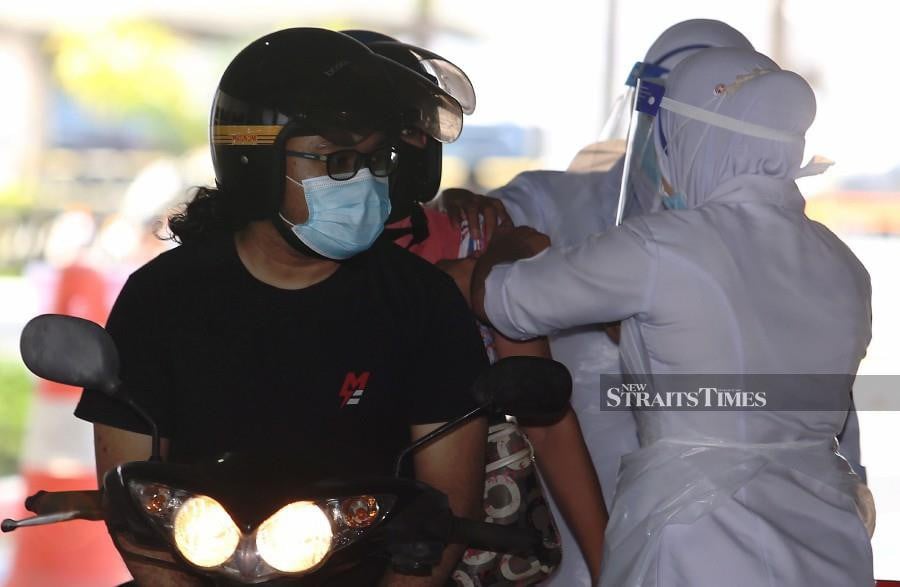 A motorist stops to get his pillion rider vaccinated at the drive-through vaccination centre (PPV) in Indera Mulia Stadium. -NSTP/SHARUL HAFIZ ZAM