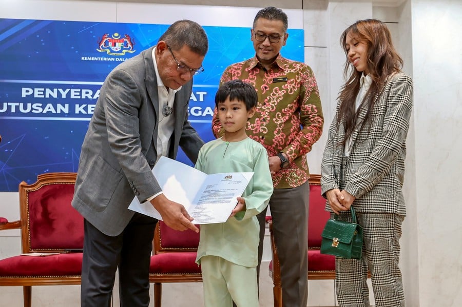 Home Minister Datuk Seri Saifuddin Nasution Ismail presenting a certificate of citizenship to 8-year-old Yusuf Alexander as his mother, Hani Azali, looks on. Bernama pic