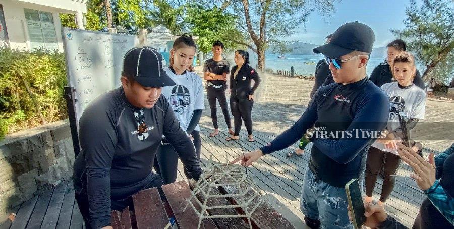 Sabah Parks staff (left) briefing divers on how to tie coral fragments using mini model of coral frames at Mamutik island during the Ocean Hero 2.0 programme yesterday. - NSTP/OLIVIA MIWIL 