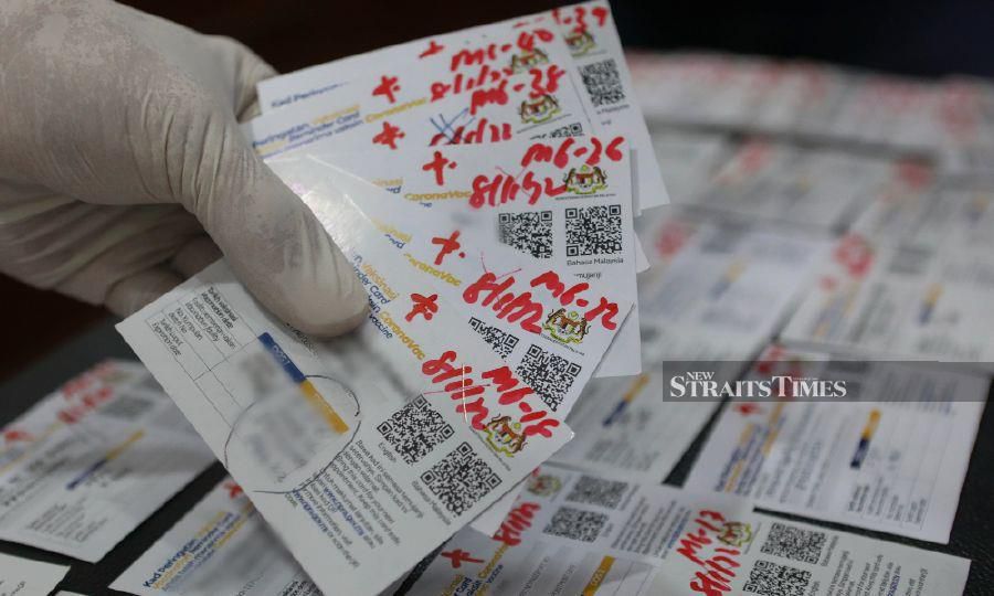 This January 10, 2022 pic shows, a police officer showing some of the fake Covid-19 vaccination certificates, during a press conference at the Terengganu police contingent headquarters in Kuala Terengganu. - NSTP/GHAZALI KORI