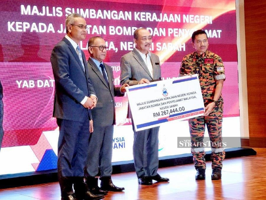 Sabah Chief Minister Datuk Seri Hajiji Noor (centre) handing over the contribution to State Fire and Rescue Department director Abdul Razak Muda. - NSTP/Paul Mu