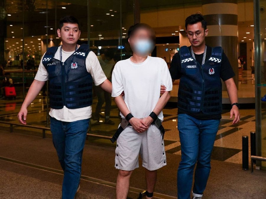Singapore Police Force officers escorting the men, who were arrested for their suspected involvement in malware-enabled scams, extradited from Malaysia. - PICS COURTESY: Singapore Police Force.