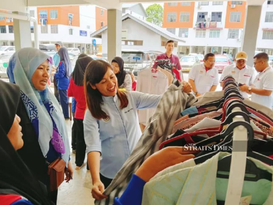 Teo Nie Ching (right) helps local residents choose free used Raya clothes donations at Flat Taman Putri here. STR/OMAR AHMAD