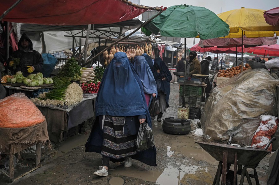 Burqa-clad women walk along a market on a cold day in Kabul. - AFP PIC