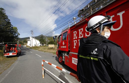 A firefighter allows a fire engine onto a restricted road leading to Mount Ontake as firefighters head to the mountain to aid in the rescue efforts of those stranded and injured, in Otaki Village, Nagano prefecture, Japan. Mount Ontake in central Japan erupted shortly before noon Saturday, catching mountain climbers by surprise and injuring at least 34, including 12 seriously, according to Japan's Fire and Disaster Management Agency. The tally was lower than reported by local officials earlier, but the disaster agency warned that the numbers could still change. AP Photo 