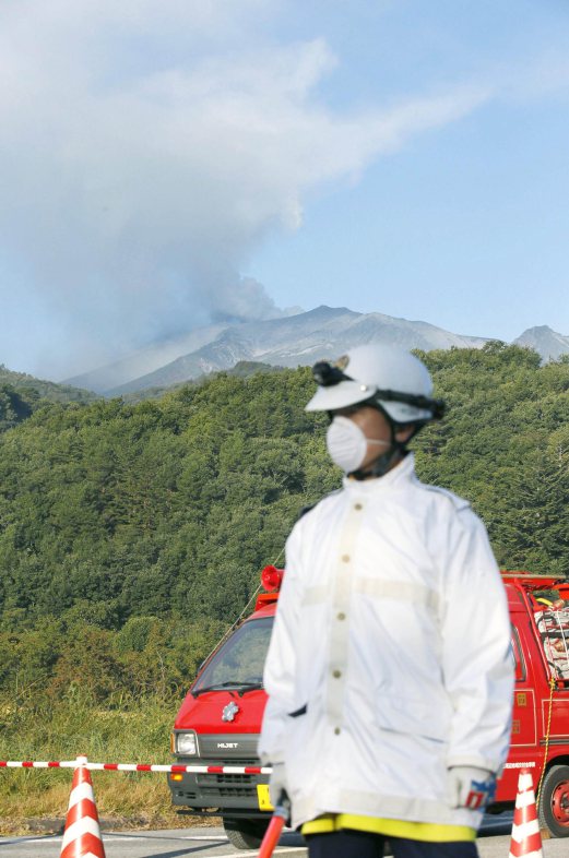 A police officer stands guard on a road to Mt. Ontake (top) at Kiso town, in Nagano prefecture, central Japan in this September 28, 2014 photo taken and released by Kyodo. More than 500 Japanese military and police set out on Sunday to search the peak of a volcano popular with hikers a day after its sudden eruption trapped hundreds on the mountain for hours, amid conflicting reports about missing and injured climbers. Mandatory credit. REUTERS/Kyodo 