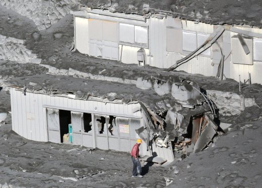 A man walks next to mountain lodges covered with volcanic ash near a crater of Mt. Ontake, which straddles Nagano and Gifu prefectures in this September 28, 2014 photo taken and released by Kyodo. More than 500 Japanese military and police set out on Sunday to search the peak of a volcano popular with hikers a day after its sudden eruption trapped hundreds on the mountain for hours, amid conflicting reports about missing and injured climbers. Mandatory credit. REUTERS/Kyodo 