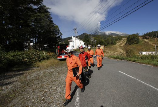 Firefighters walk down a road headed away from Mount Ontake, background right, as it continues to erupt Sunday, Sept. 28, 2014, in Otaki Village, Nagano prefecture, Japan. Mount Ontake in central Japan erupted shortly before noon Saturday, catching mountain climbers by surprise and injuring at least 34, including 12 seriously, according to Japan's Fire and Disaster Management Agency. The tally was lower than reported by local officials earlier, but the disaster agency warned that the numbers could still change. AP Photo 