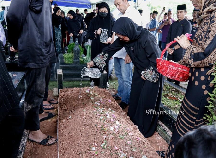 Toh Puan Hamidah Abdul Hamid pours rose water during the funeral of the late Tun Mohammed Hanif Omar at the Bukit Kiara Muslim Cemetery. -NSTP/SADIQ SANI
