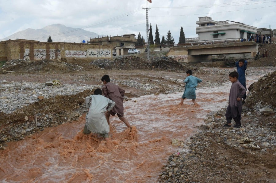 Children wade through floodwater near a damaged road following heavy rains on the outskirts of Quetta. - AFP PIC