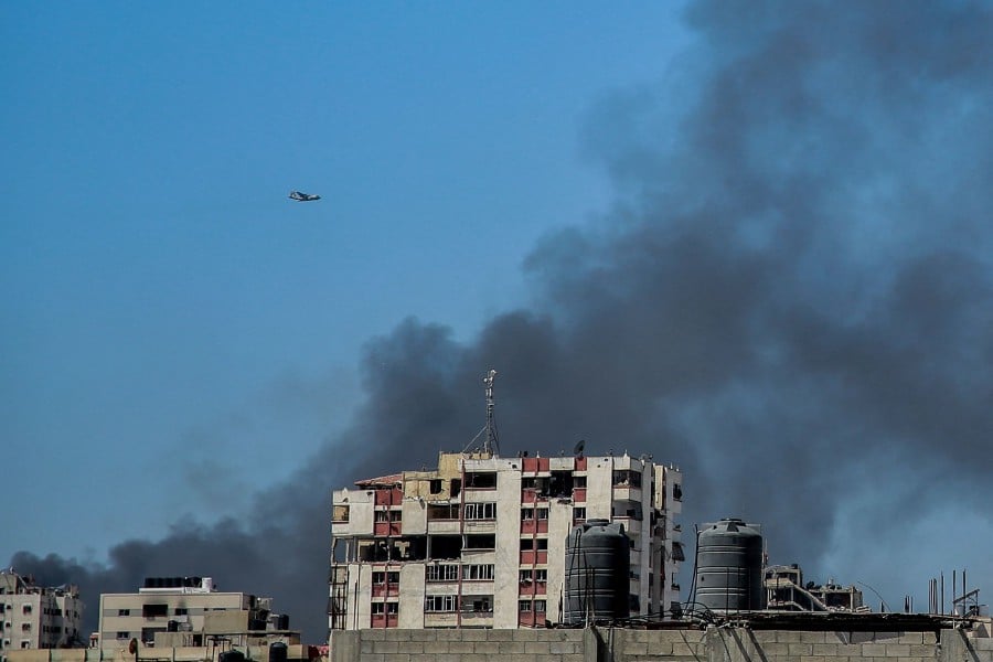 Smoke rises above the Rimal district in Gaza City as a military aircraft prepares to airdrop humanitarian aid on March 20, 2024. - AFP PIC