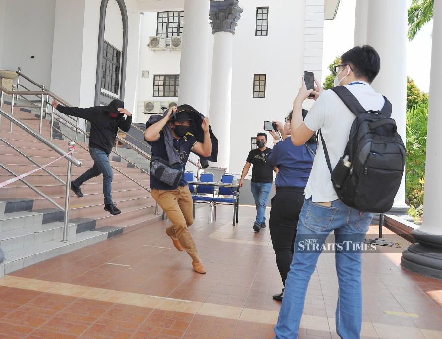  Amir Izham Shahak (front) and Wan Kamarul Za'im Wan Mansor (back) trying to evade pressmen after the trial at the Johor Baru Session’s Court in Johor. - NSTP/NUR AISYAH MAZALAN
