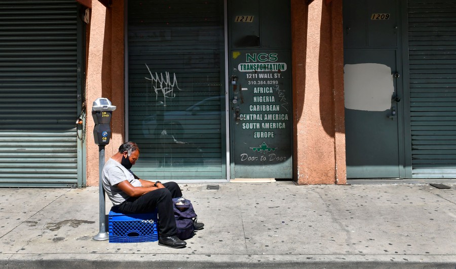 A man sleeps in front of closed shopfronts in what would be a normally busy fashion district in Los Angeles, California. - AFP