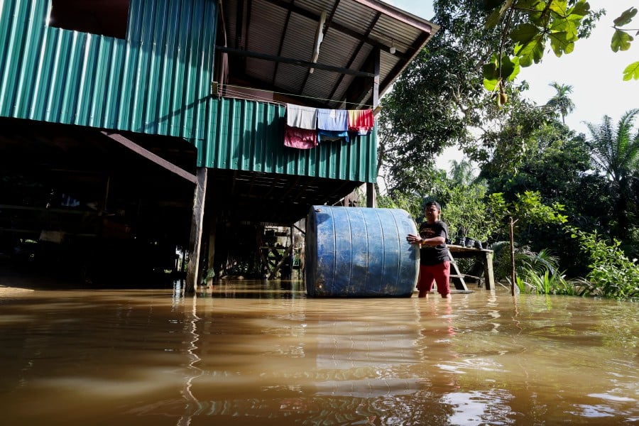 A resident in Sandakan, pushes a water tank which was swept away during the floods in Kampung Sungai Memanjang. - BERNAMA PIC