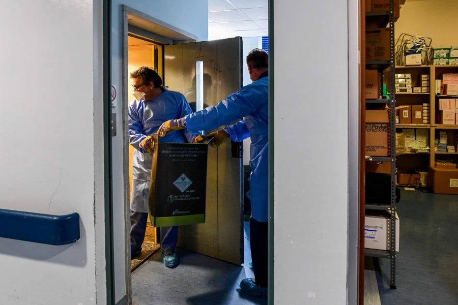 Employees of the Cremona Territorial Healthcare Company (ASST) dispose of hospital waste stored in a special cardboard box on April 27, 2020 at the COVID-19 ward of the Cremona hospital, Lombardy. - AFP