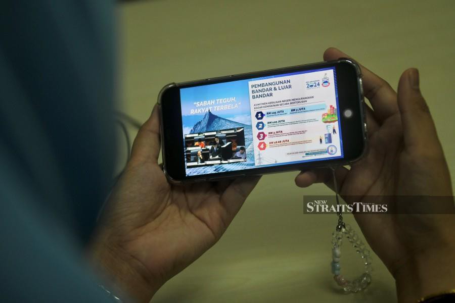 A civil servant watches the tabling of Sabah’s 2024 Budget on a smartphone in Kota Kinabalu. -NSTP/MOHD ADAM ARININ