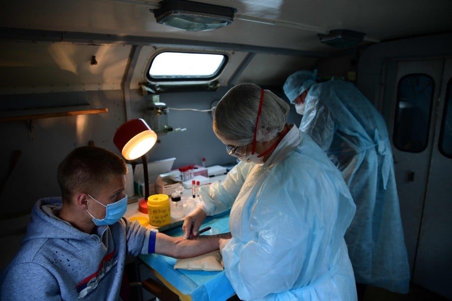  A medical specialist wearing protective equipment takes a blood sample from a conscript during a rapid test for the COVID-19 novel coronavirus at a recruiting office in the far eastern city of Vladivostok on June 4, 2020.- AFP pic
