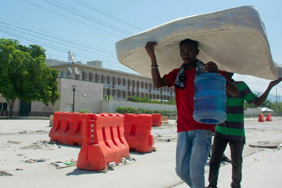 Two person carrying a mattress as they walk past the US embassy in Port-au-Prince, Haiti, on March 12, 2024. -- Pic: AFP