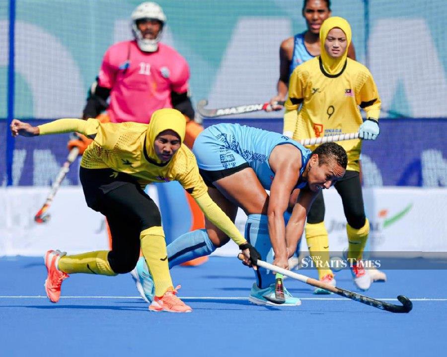 A Malaysia player (in yellow) tries to stop a Fiji player in a women's Hockey 5s World Cup match in Muscat, Oman, today. 