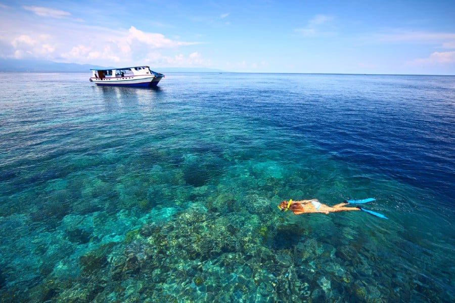 Young woman in swimsuit snorkeling in blue and transparent tropical sea not far away from a boat.- File pic